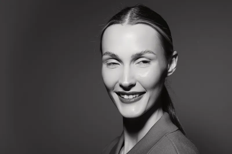Close-up portrait of smiling white woman with pale skin and dark hair pulled back. Studio black and white photography with soft lighting and shadow. Concept of happiness and beauty.