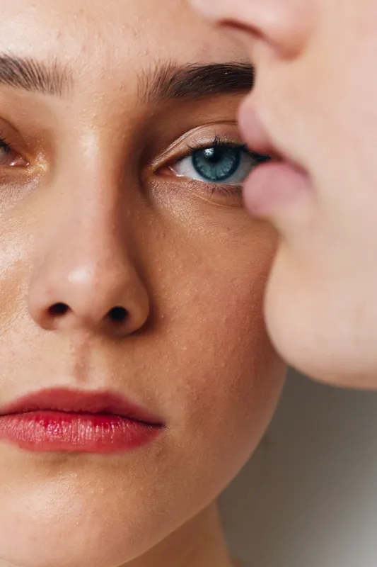 Closeup portrait of two women with natural skin and blue eyes, showing detailed facial features, lips with red lipstick and smooth complexion in soft lighting.