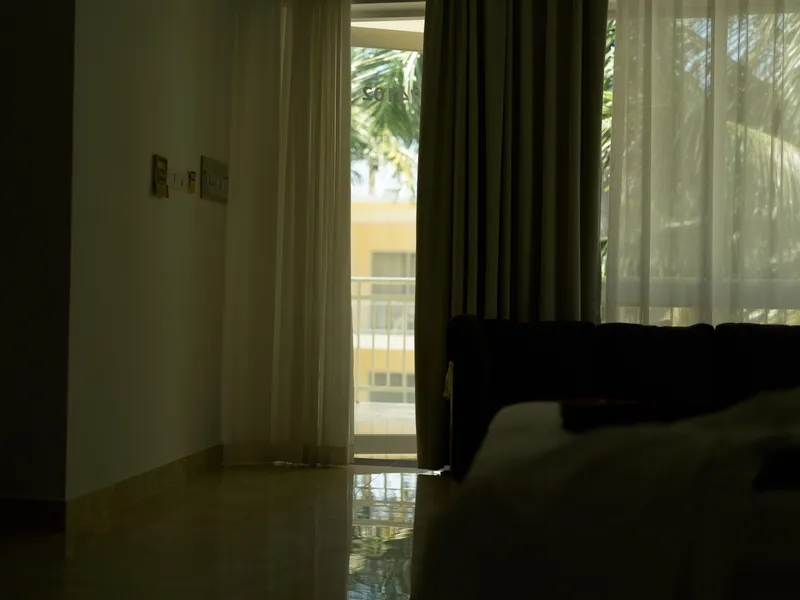 Dark interior of a modern room with sheer curtains partially drawn, soft natural light filtering through the window, creating a calm and quiet atmosphere.