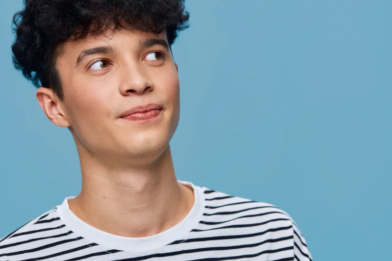 young man wearing striped shirt looking thoughtful on blue background with soft lighting, capturing casual mood and natural expression
