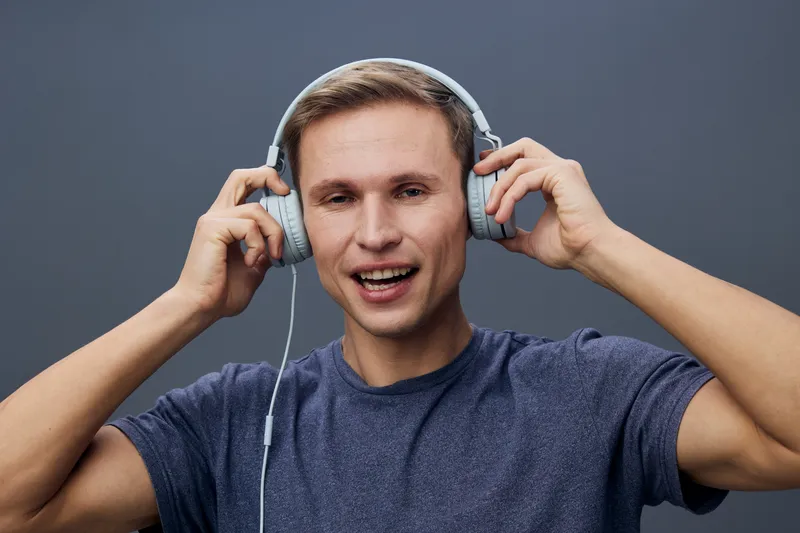 Smiling young man wearing casual navy t-shirt in headphones listening to music isolated on plain gray background. People lifestyle concept, happiness, leisure, relaxation, entertainment, modern techno