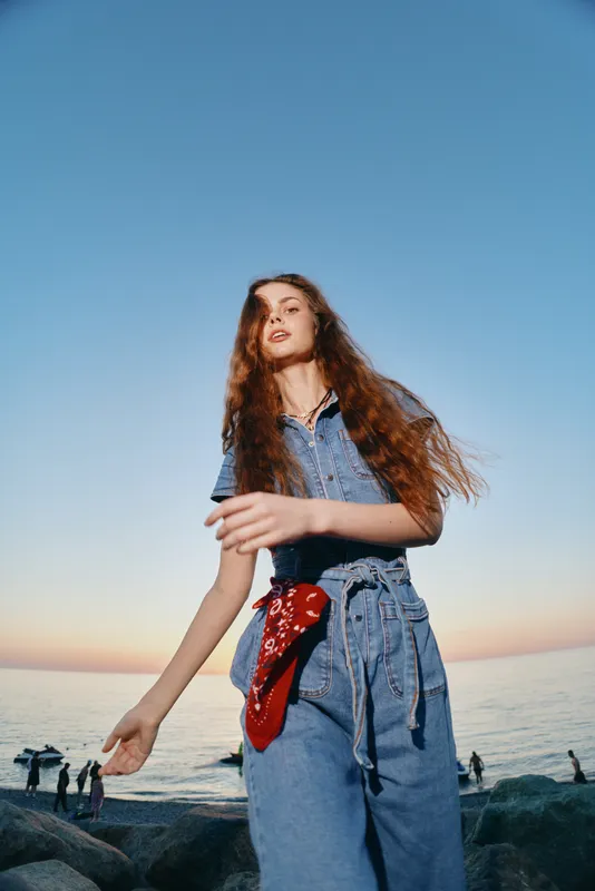Lifestyle woman in modern boho-western denim street style with flowing hair outdoors near the sea, film color effect enhancing natural sunlight and relaxed mood.