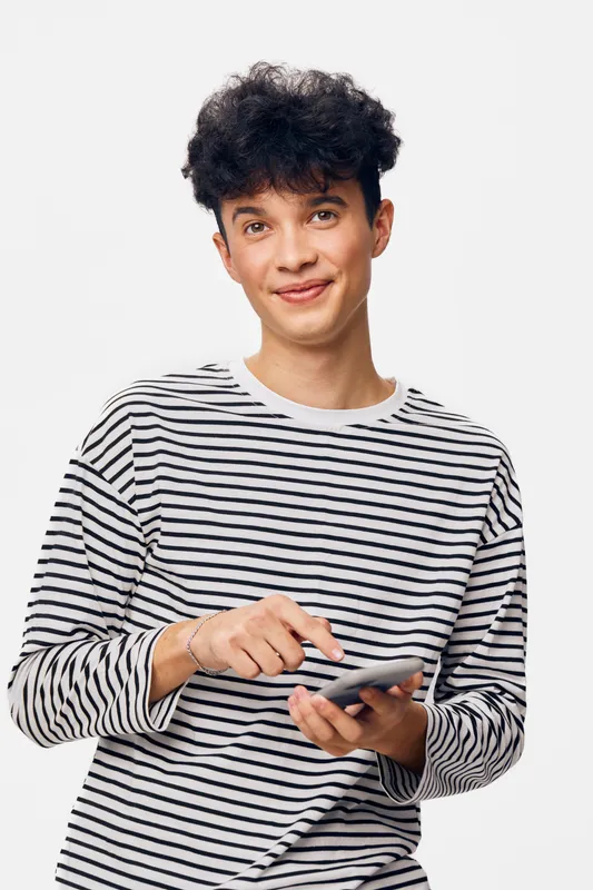 young man with smartphone smiling softly wearing striped shirt isolated on white background, casual style, curly hair, positive emotion, modern technology use