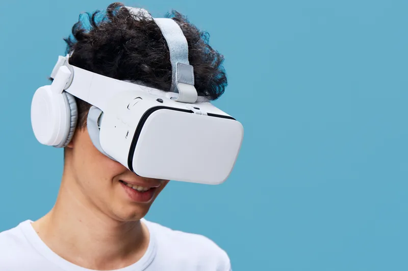 young man wearing white virtual reality headset and headphones smiles enjoying immersive digital experience against light blue background in modern technology concept