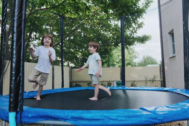 Two joyful boys having fun on a trampoline, enjoying outdoor play in a cheerful atmosphere surrounded by greenery and sunlight.
