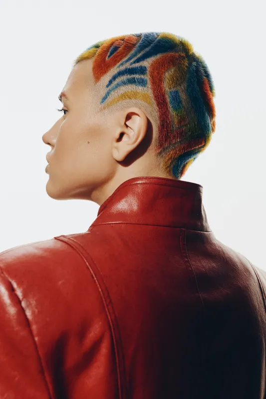 woman with colorful short hair in artistic pattern wearing red leather jacket, side profile, creative hairstyle, modern fashion, minimal white background