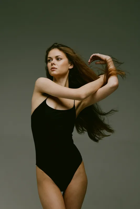 young woman in black swimsuit posing with flowing hair in studio, portrait of confident female beauty and elegance