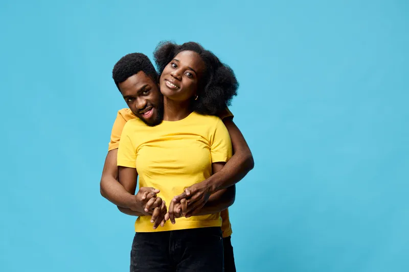 Happy couple embracing against a vibrant blue background, showcasing love and joy in matching yellow outfits Perfect for concepts of relationships and romance