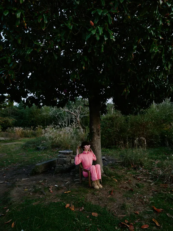 Child girl in pink sits under a large tree in an outdoor park, enjoying shade and calm as leaves fall around. A peaceful, innocent moment of nature and quiet reflection.
