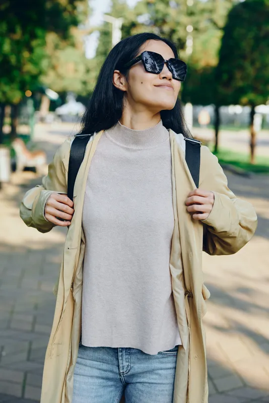 Outdoors fashion style with a confident woman wearing a trench coat, knit sweater and sunglasses in a sunny park, showcasing casual chic streetwear and lifestyle.