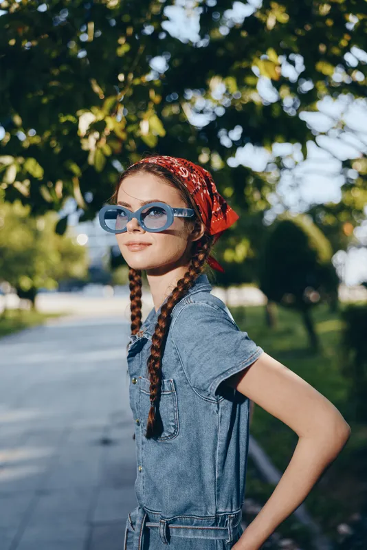 lifestyle woman in modern boho-western denim street style wearing blue sunglasses and red bandana with natural outdoor background, film color aesthetics.