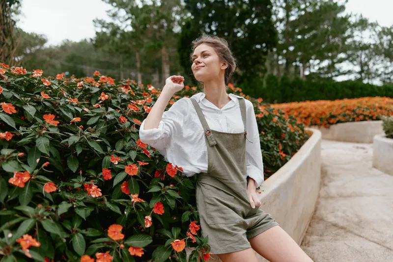 Young woman enjoying a sunny day in the park surrounded by vibrant flowers, wearing a casual outfit and exuding a carefree and joyful emotion in a fresh spring environment