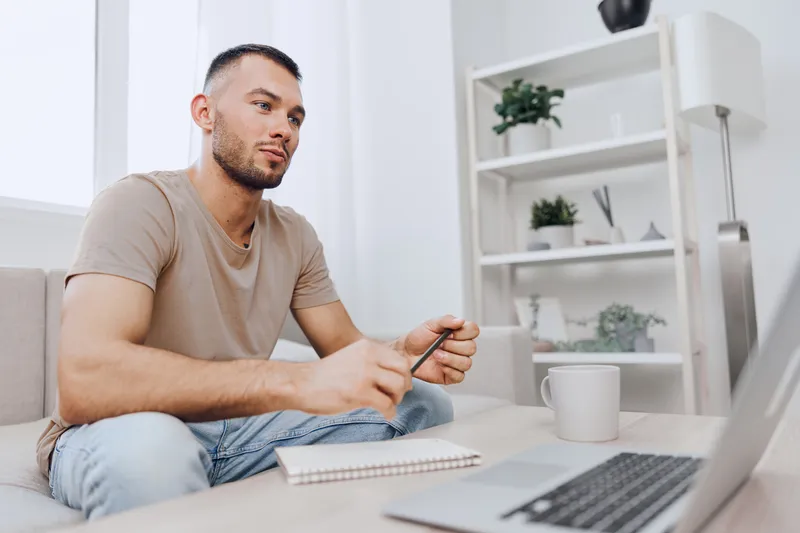 Thoughtful man analyzing data while working remotely in a modern living room, featuring a cozy atmosphere and stylish decor elements with indoor plants.