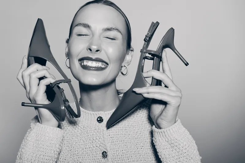 Smiling white woman with fair skin holding pair of high heel shoes near face with closed eyes. Concept for fashion, footwear, happiness, and lifestyle in studio lighting.