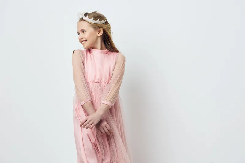 Charming young girl in a pink dress with long sleeves, smiling joyfully against a light background, perfect for children s fashion and celebrations