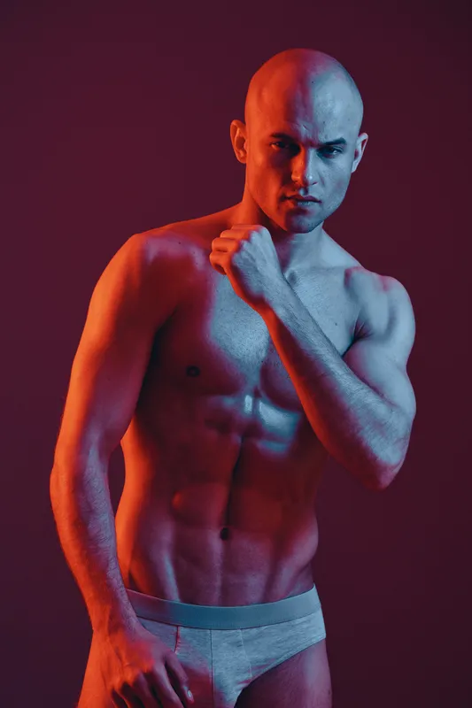 Athletic man posing with a confident expression, showcasing his physique against a vibrant gradient background. Black and white image emphasizing strength and mood.
