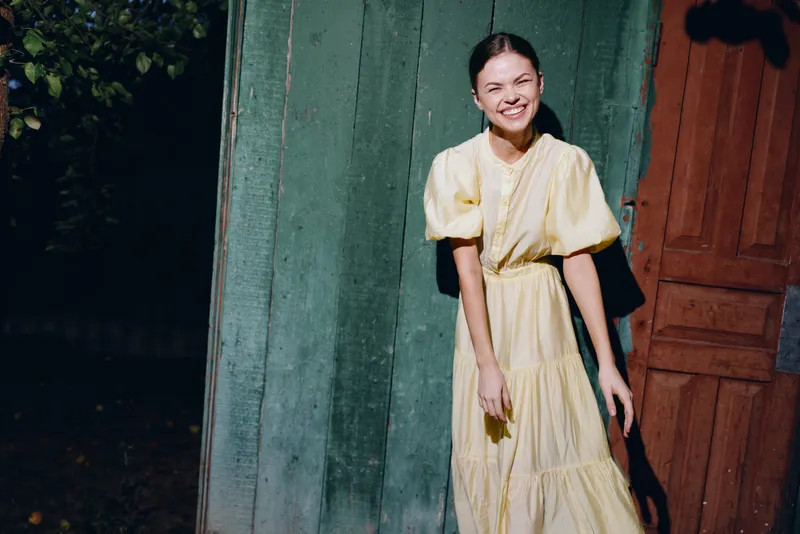 Woman portrait of a cheerful figure in a yellow dress beside a doorway, outdoor setting with a bright smile, fashion mood and sunshine.