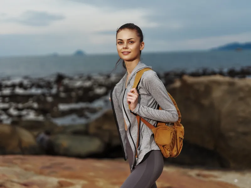 Young woman hiking in comfortable athletic wear on a rocky beach, displaying confidence and enjoying nature Perfect for outdoor activity themes, travel, and fitness