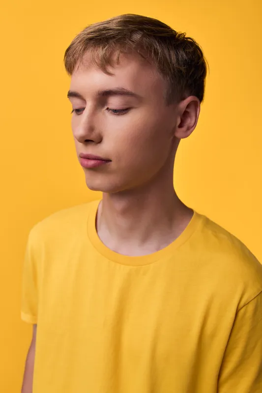 Calm young man with closed eyes wearing a yellow shirt against a bright yellow background, minimal studio setup conveying serenity, focus, and introspection
