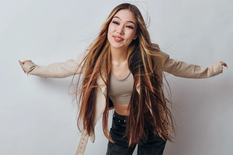 Young woman smiling with long hair wearing casual clothes and jacket posing with arms extended for fashion, beauty and lifestyle studio portrait on white background.