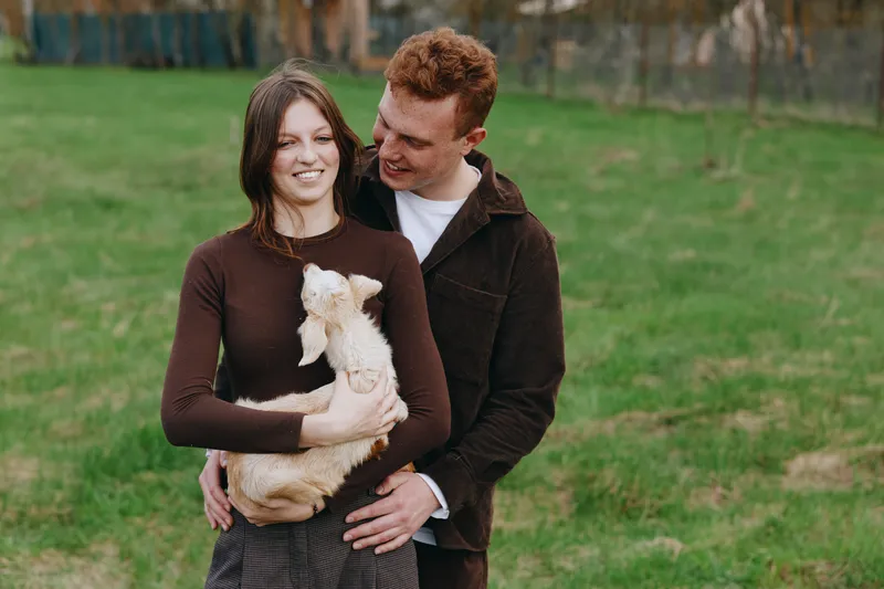 A couple outdoors warmly embrace their small dog in a sunny park setting, showcasing everyday love, companionship, and a relaxed lifestyle, with soft colors, candid moment, gentle affection, peaceful