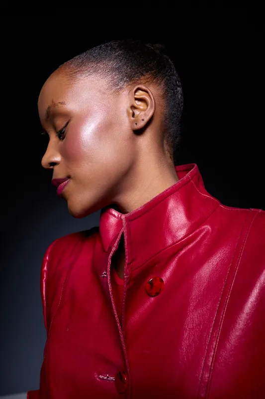 Profile of an elegant black woman with dark skin wearing a red leather jacket against a black background. Concept of fashion, beauty, confidence, and style in studio lighting.