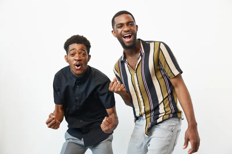 Two joyful African American men celebrate with excitement, showcasing emotions of happiness and camaraderie. Bright colors enhance the lively atmosphere and positive energy.