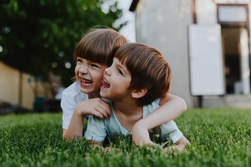Playful children enjoying outdoor fun, embracing each other on the green grass in a sunny atmosphere. Their laughter radiates joy and innocence.