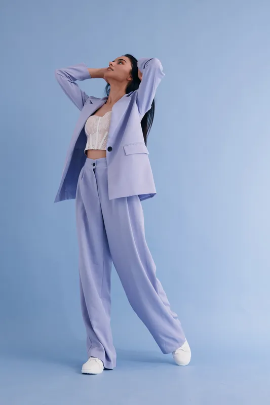 young woman in lavender suit and white lace top posing against blue backdrop, stylish outfit, casual elegance, minimalistic studio setting with soft lighting