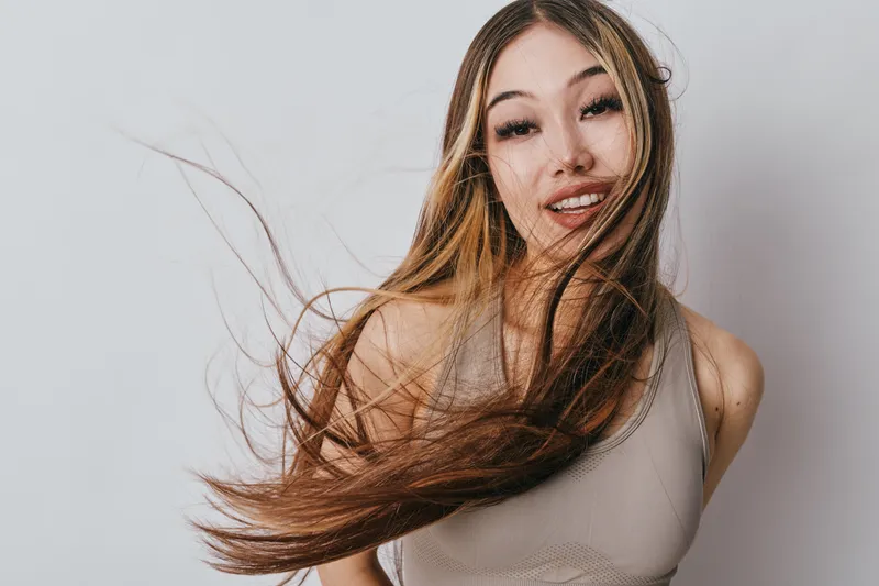 Young woman with long hair smiling and turning head, casual style with movement and natural look, portrait on light background with dynamic hair flow.