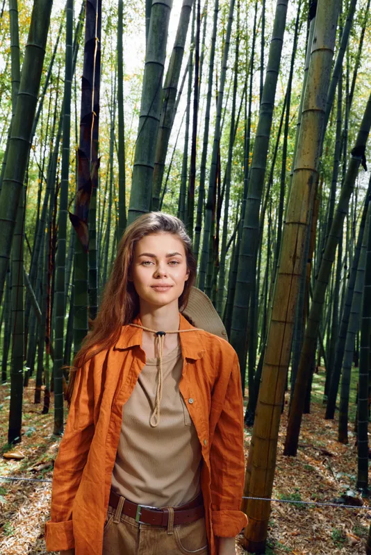 Woman bamboo forest portrait, traveler with backpack and orange jacket standing among tall green stalks, nature scene and serene outdoors mood for adventure and exploration.