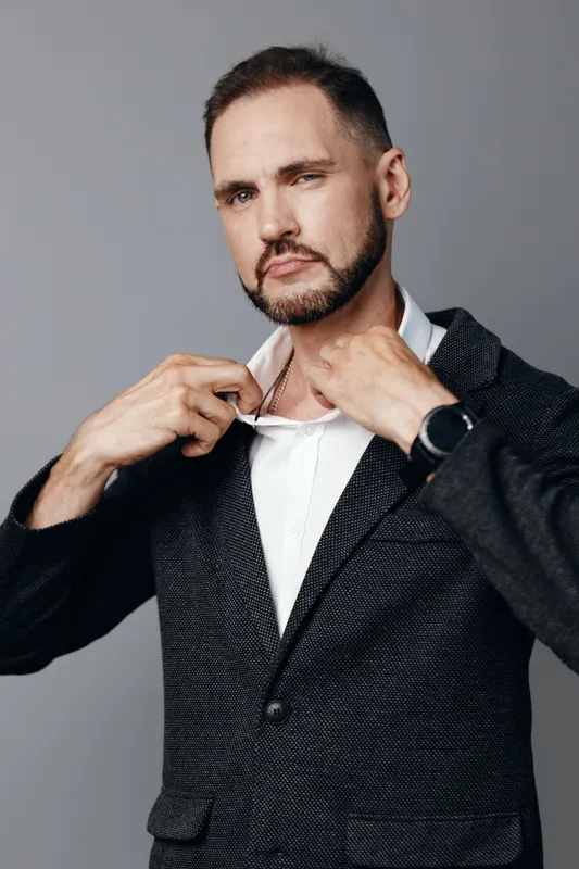 A professional businessman stands against a plain colored background, projecting confidence and calm while adjusting his suit, ready for a focused corporate moment.