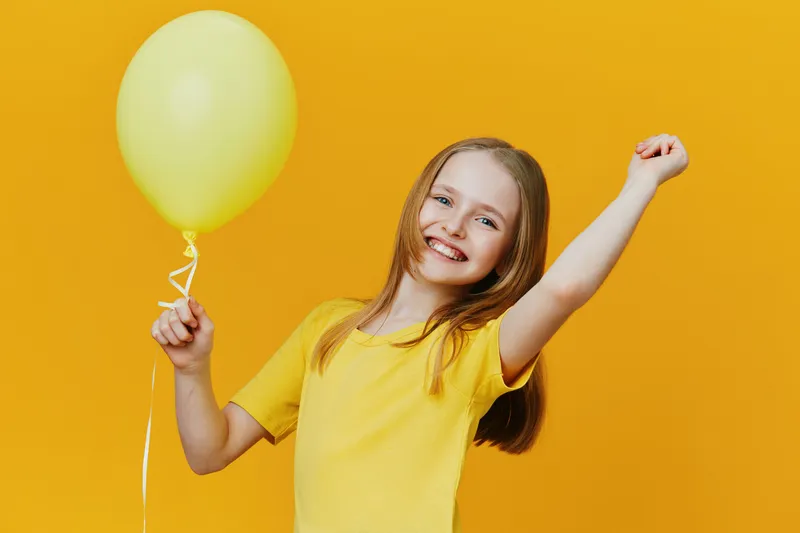 Happy girl in a bright yellow shirt holding a yellow balloon, celebrating joy and positivity against a vibrant yellow background