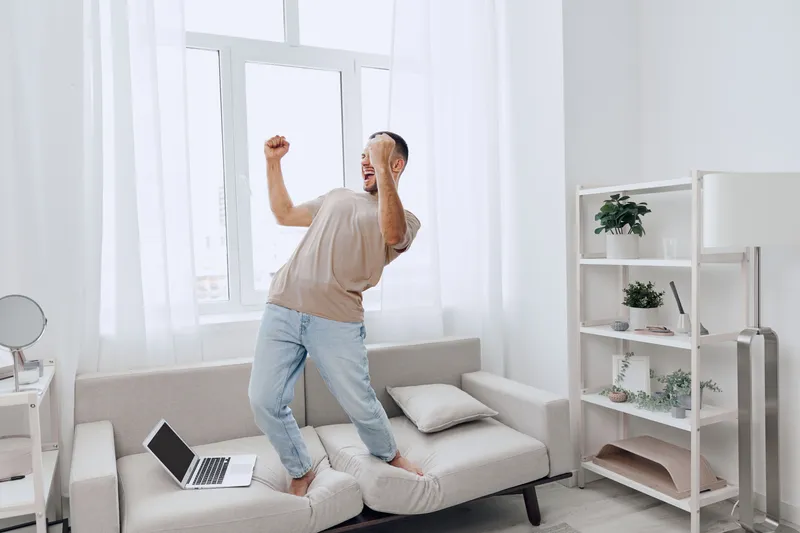 Energetic man celebrating a moment of victory at home, blending personal and work life while enjoying a break from technology. Concept: joy of living authentically.