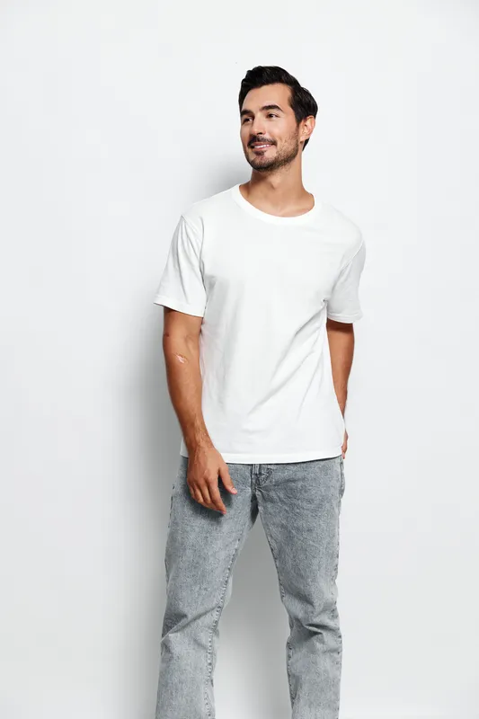 Stylish young man wearing a plain white t-shirt and gray denim jeans, stands confidently with a friendly smile against a neutral background. Casual lifestyle concept.