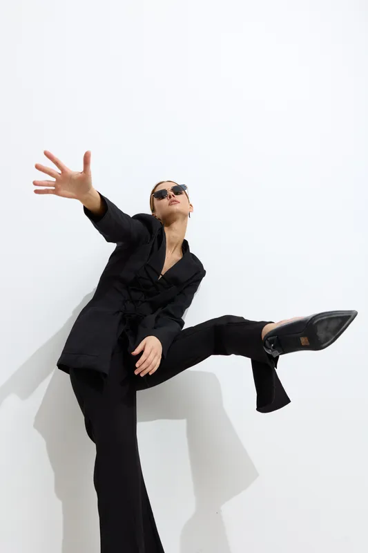 fashion woman in black suit wearing sunglasses posing dynamically against white background, stylish and modern, confident attitude in studio lighting