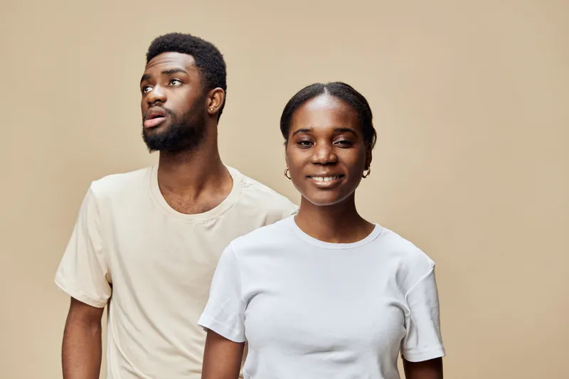 A cheerful young African couple wearing casual white t shirts against a neutral beige background, showcasing positivity and connection through their expressions