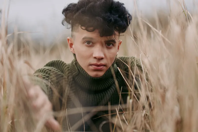Close-up portrait of a young adult in tall dry grass, conveying a genuine unposed moment with natural expression and simple wardrobe, emphasizing realism and a trustworthy documentary aesthetic.