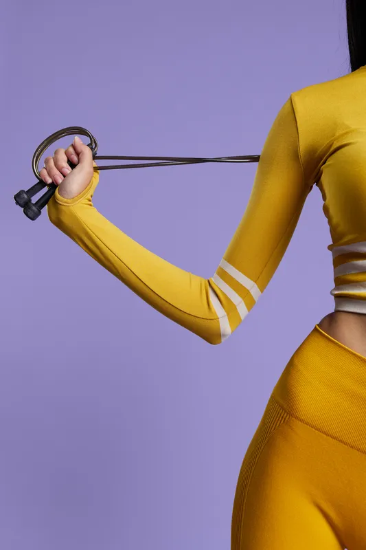 Woman sport fitness exercising with resistance band in yellow activewear, dynamic pose with purple background, healthy lifestyle and strength training concept.