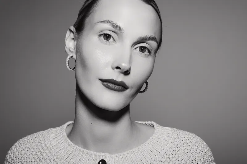 Closeup portrait of a fair skinned white woman with short hair wearing earrings and a knit sweater posing against a plain studio background. Concept of elegance and simplicity.