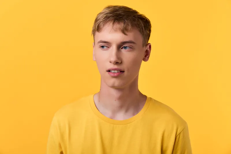 Young man, yellow shirt, yellow background, casual pose, contemplative look, clean lighting, modern fashion, bright colors, studio shot, minimalism, relaxed mood, simple styling, warm tone