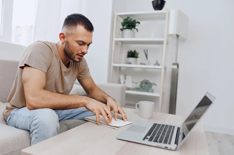 Focused man working from home on a laptop, creatively engaged in his tasks. Stylish indoor environment, with soft natural light and cozy decor.