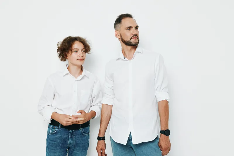 Professional man stands with calm confidence against a clean white backdrop, projecting business focus and emotion, while a younger colleague supports teamwork and leadership for corporate use and