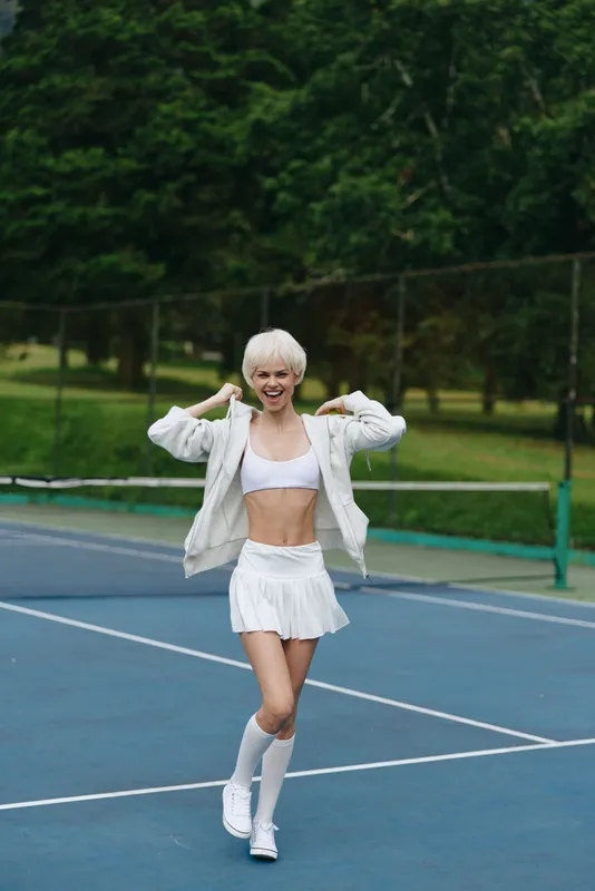 Energetic female athlete in stylish sportswear enjoying a sunny day on a tennis court, showcasing confidence and joy while promoting an active lifestyle