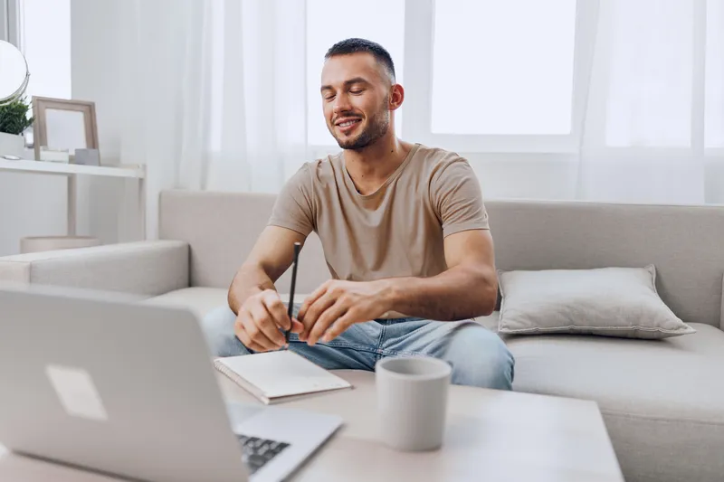 Smiling man working at home, engaging in online learning and personal development, surrounded by a cozy and minimalistic atmosphere, embracing modern lifestyle trends.