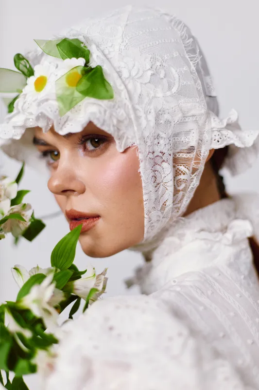Elegant young woman in a vintage white dress, adorned with flowers, exuding a serene expression, showcasing delicate beauty and spring themes