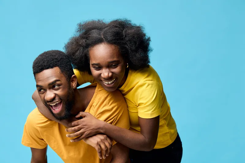 Happy African couple joyfully enjoying time together against a bright blue background, wearing matching yellow shirts, showcasing love and friendship