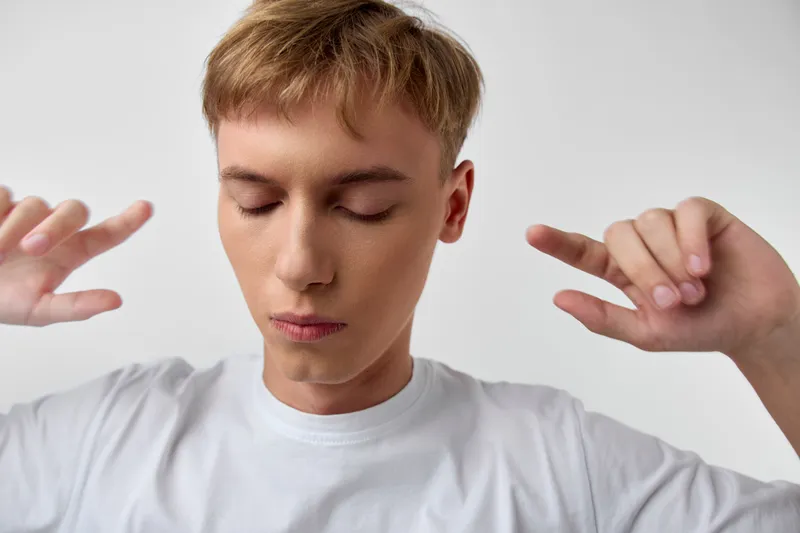 Meditation scene with a young man, eyes closed, hands raised in a relaxed pose, depicting calm focus and inner balance during mindful breathing and mental clarity in a simple studio setting