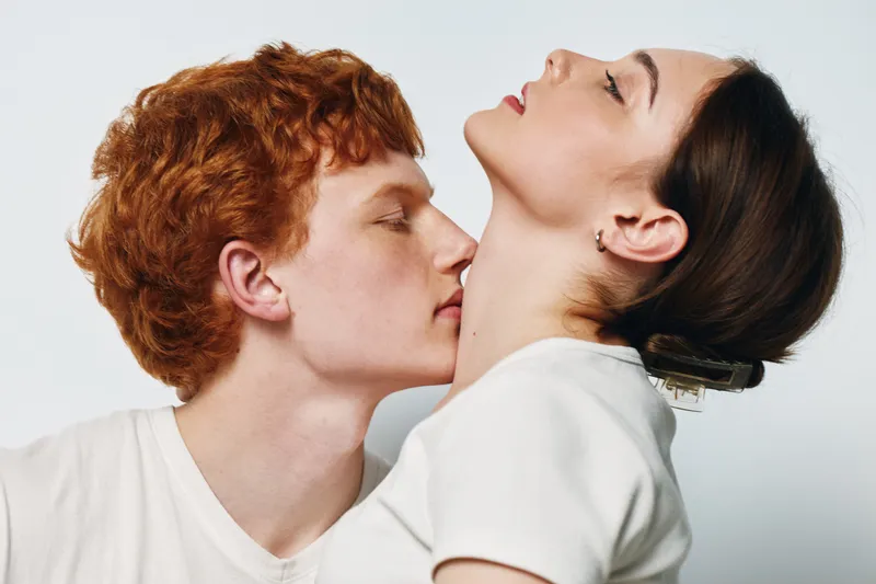 Couple, intimacy and affection with man kissing woman neck in closeup, romance and connection between young people with white background and casual clothes in studio shot portrait.