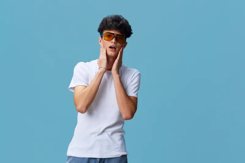 young man wearing sunglasses and white t-shirt with surprised expression on blue background, casual style, summer mood, isolated